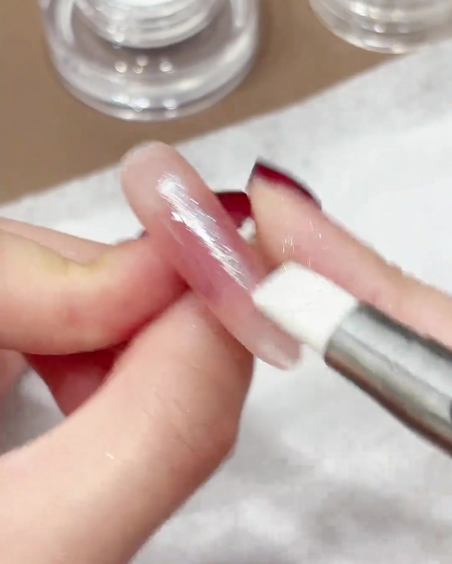 Ein Silikonstift arbeitet irisierendes Chrome-Puder in die Oberfläche eines manikürten Nagels ein.