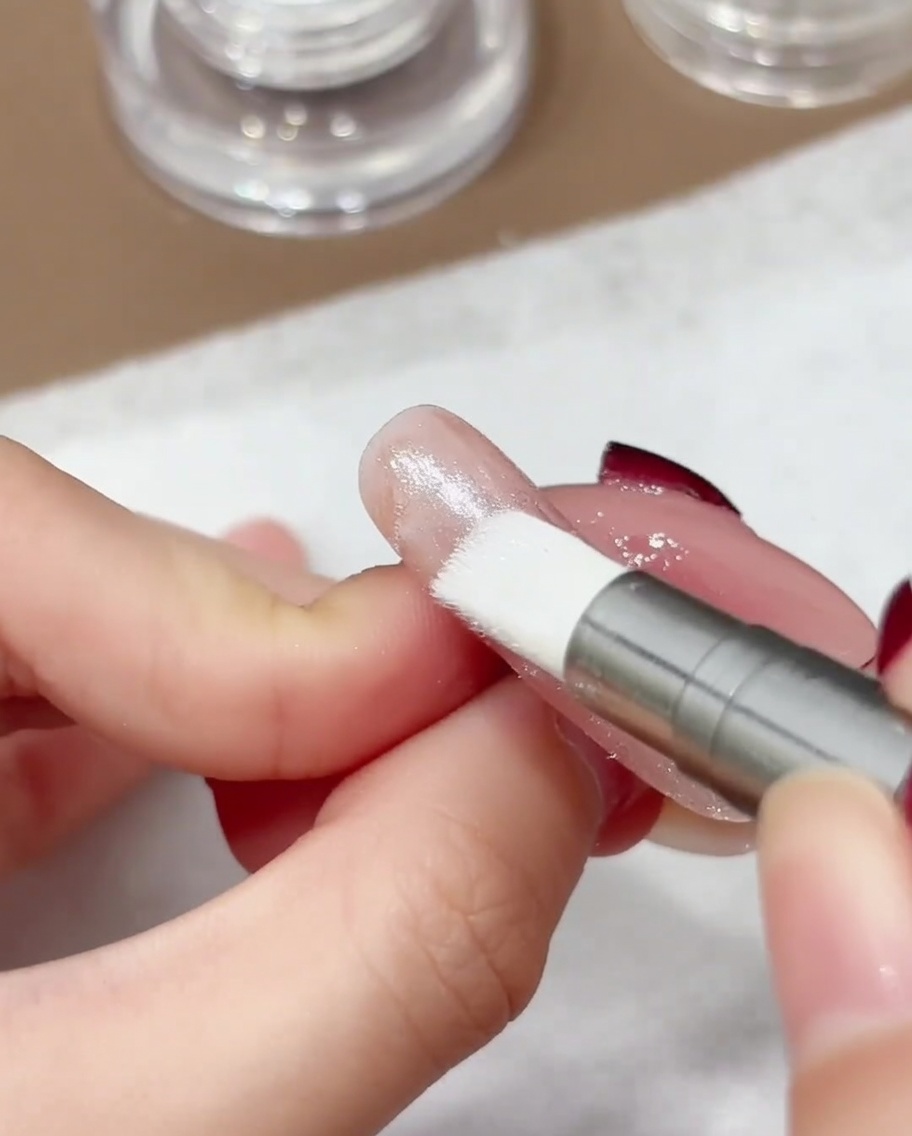 Nahaufnahme eines Silikon-Applikators, der irisierendes Aurora-Chrome-Puder in eine Nageloberfläche einarbeitet.