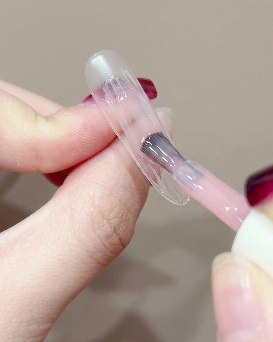 Nahaufnahme eines Gelpinsels, der einen kleinen Tupfer pfirsichfarbenes Gel in die Mitte eines nackten Nagels aufträgt.