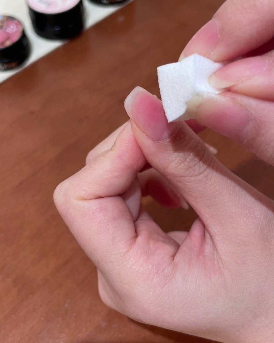 Ein Make-up-Schwamm wird verwendet, um pfirsichfarbenes Gel in einen sanften Verlauf auf der Nageloberfläche zu tupfen und zu verblenden.