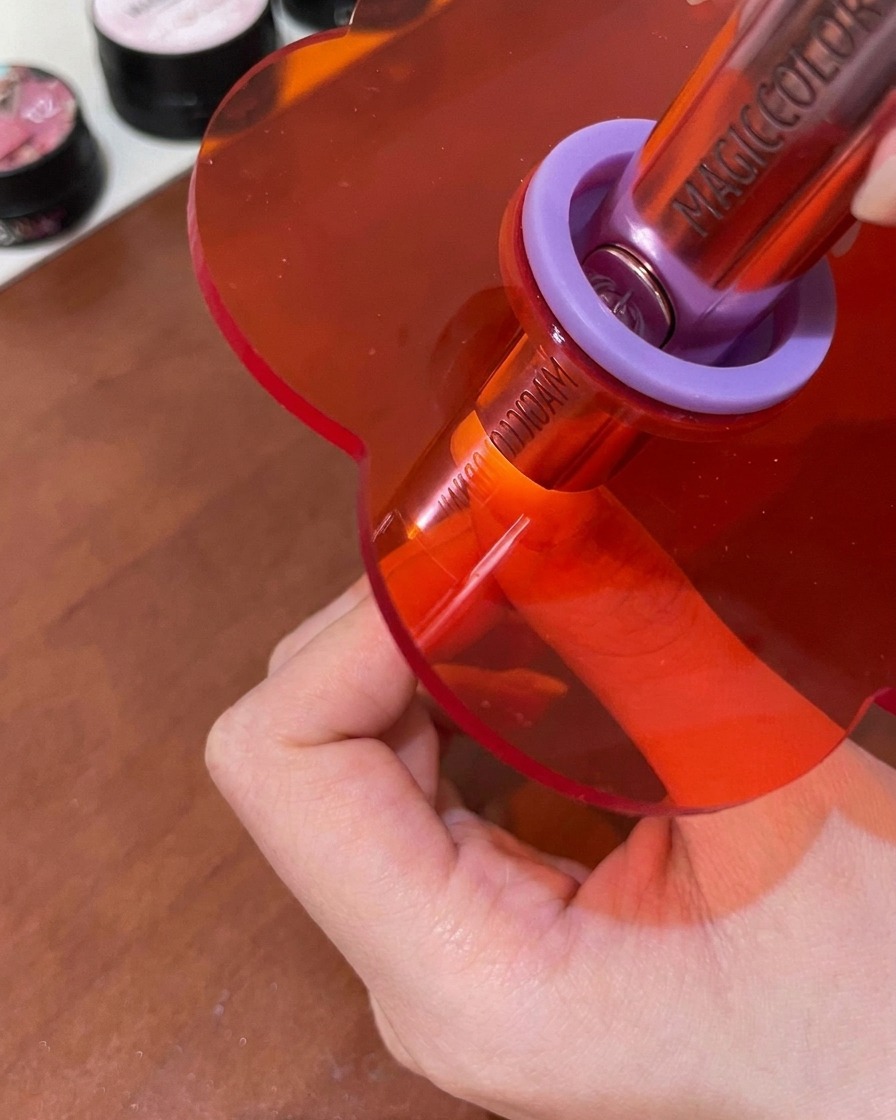 Ein Nagel härtet unter einer kleinen, handgehaltenen rosa UV/LED-Lampe aus.