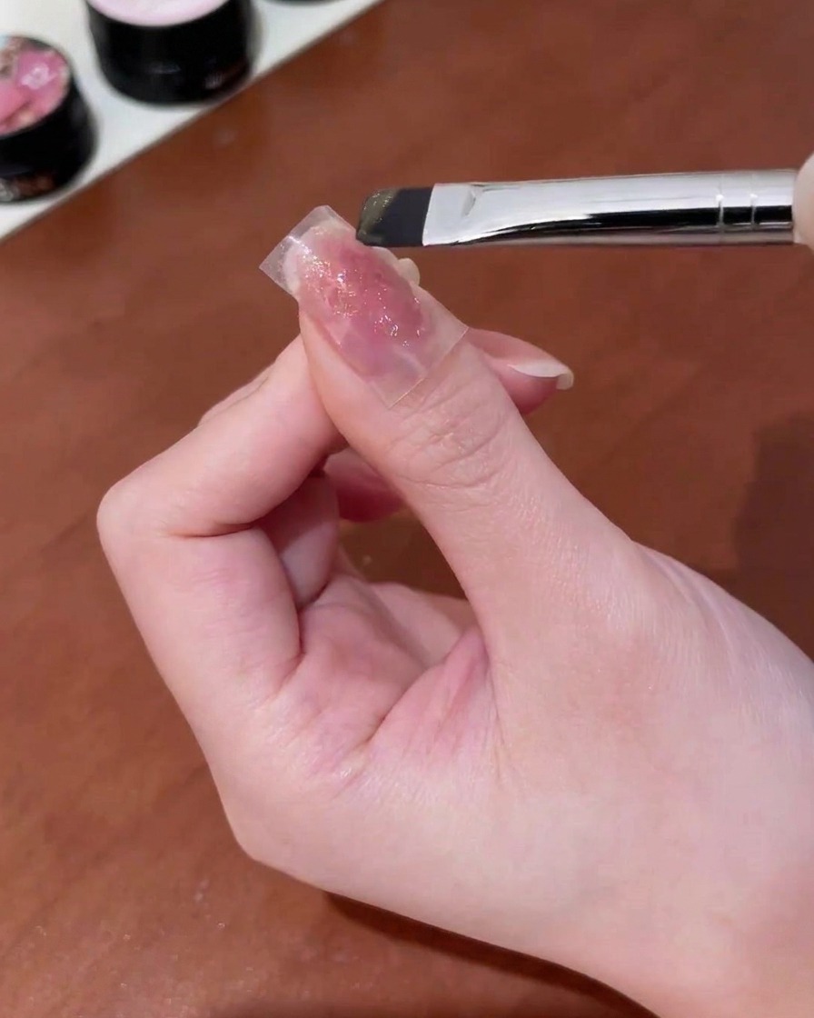 Ein Pinsel trägt goldenes Cat-Eye-Gel über einem Schmetterlingsaufkleber auf einem Nagel auf.
