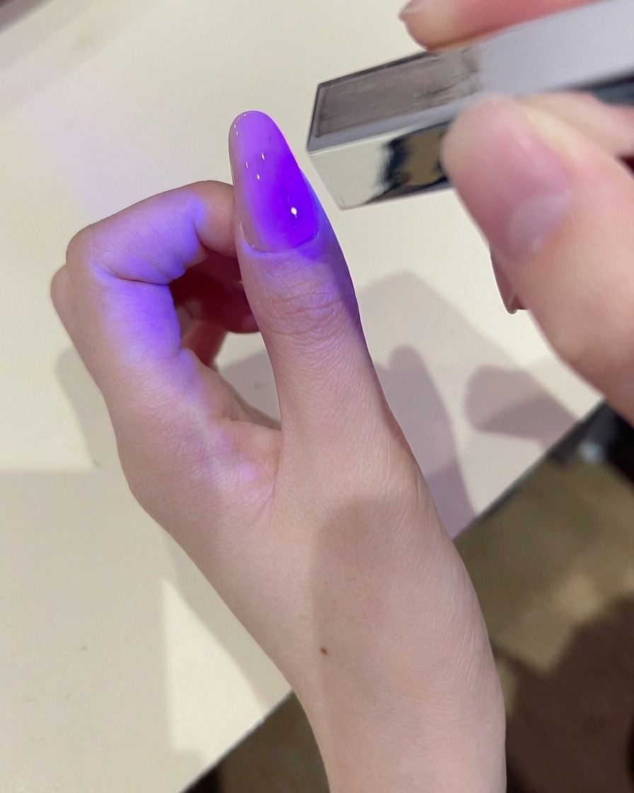 Eine Hand reinigt die Oberfläche eines ausgehärteten Gelnagels mit einem fusselfreien Tuch.