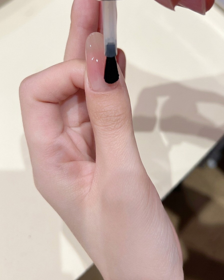 Ein Nagelpinsel trägt eine dünne Schicht klares, glänzendes Gel über den Nagel mit Blush-Zentrum auf.