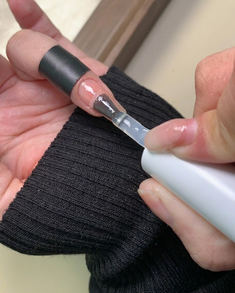 Eine Bürste trägt eine klare Schicht Basis-Gel über das fertiggestellte Aurora-Puder-Verlaufsdesign auf.
