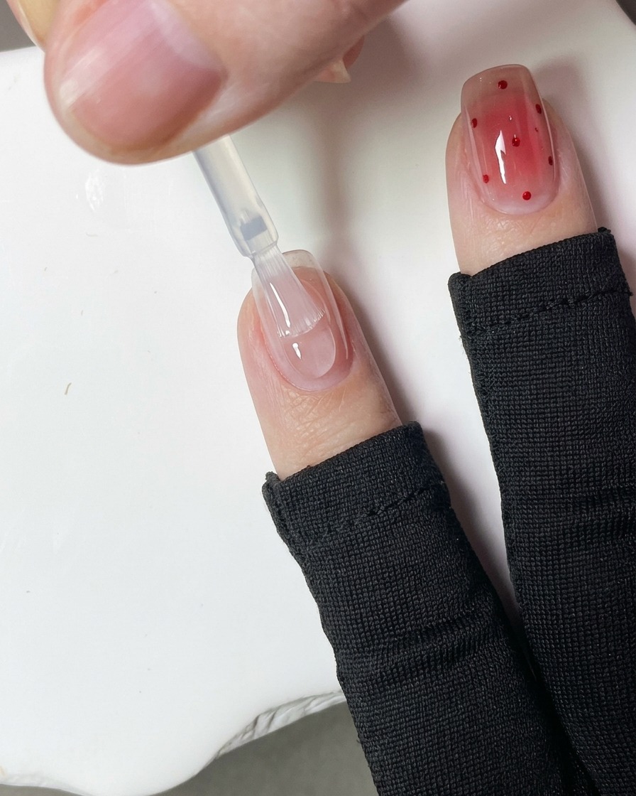 Nahaufnahme eines Dotting-Tools, das kleine rote Gelpunkte auf eine Nageloberfläche aufträgt.