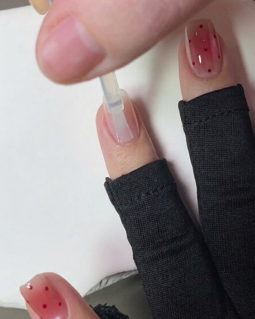 Eine Hand mit frischen rot gepunkteten Nägeln härtet in einer UV-Nagellampe aus.