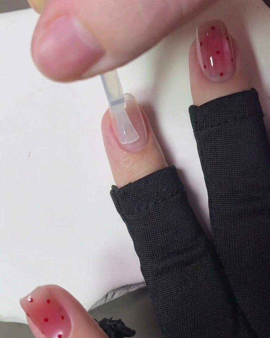 Ein Pinsel trägt einen klaren, glänzenden Überlack über die fertige Strawberry-Punkt-Nail-Art auf.