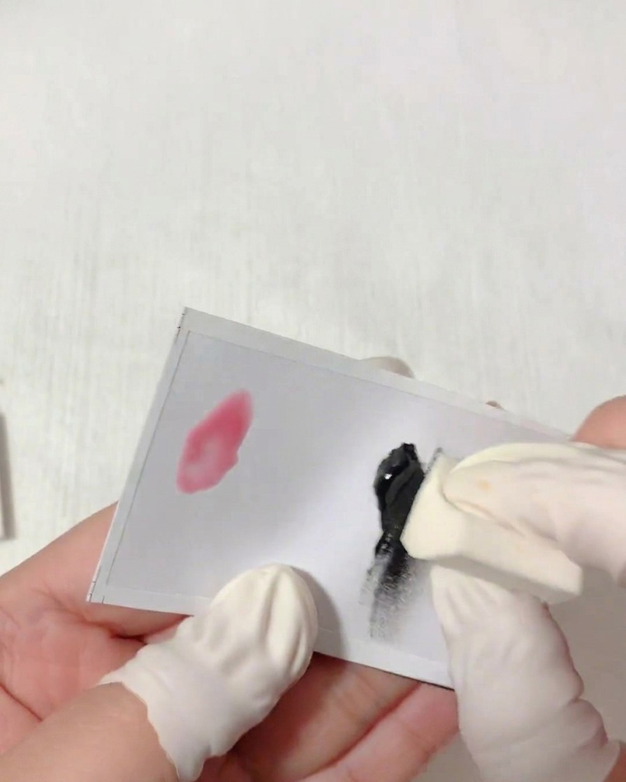 Eine Hand mit Fingerschutz tupft einen dreieckigen Schwamm in schwarzes Gel auf einer weißen Palette.