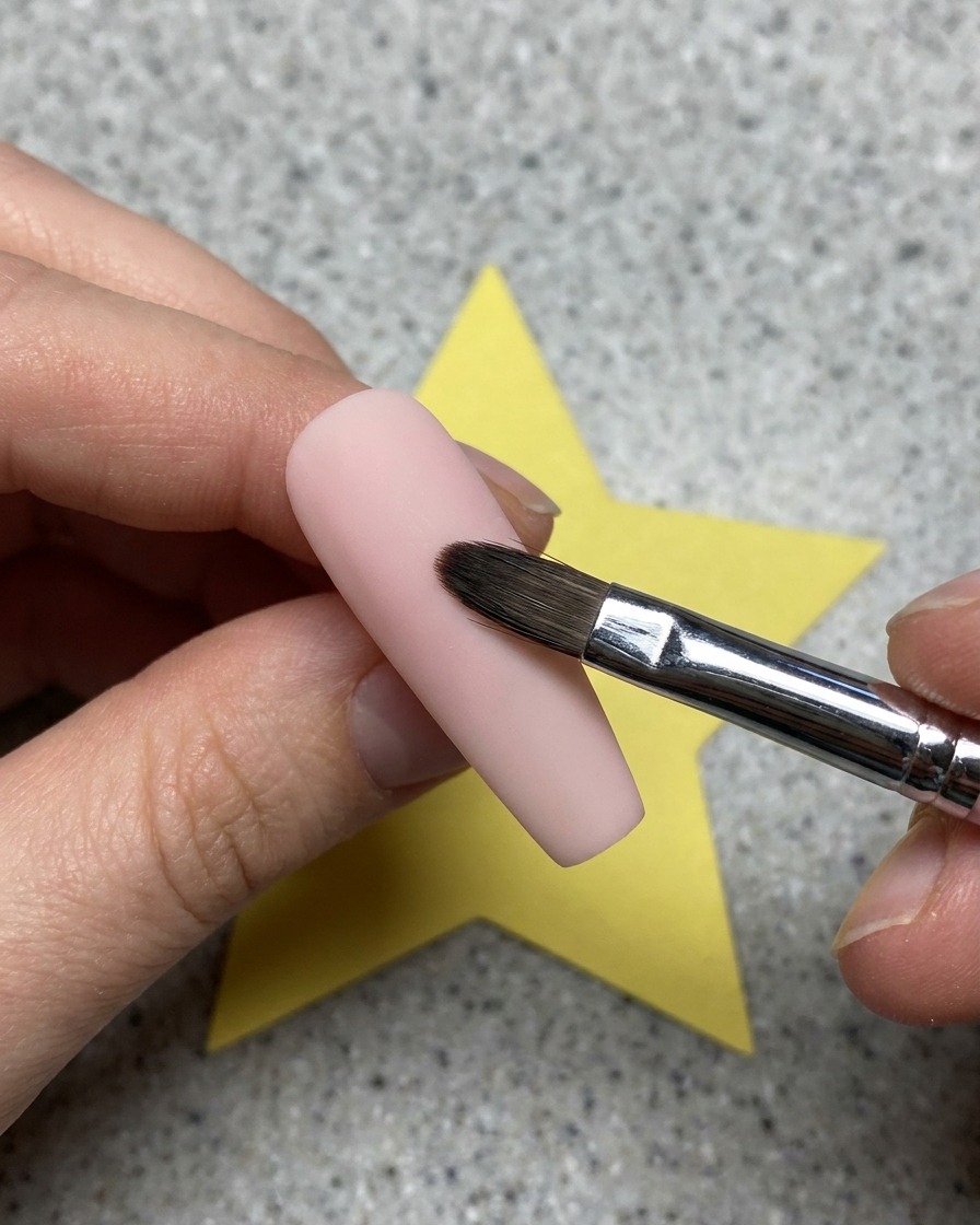 Nahaufnahme eines klaren Gels, das mit einem Pinsel über einer rosa Nagelbasis aufgetragen wird.