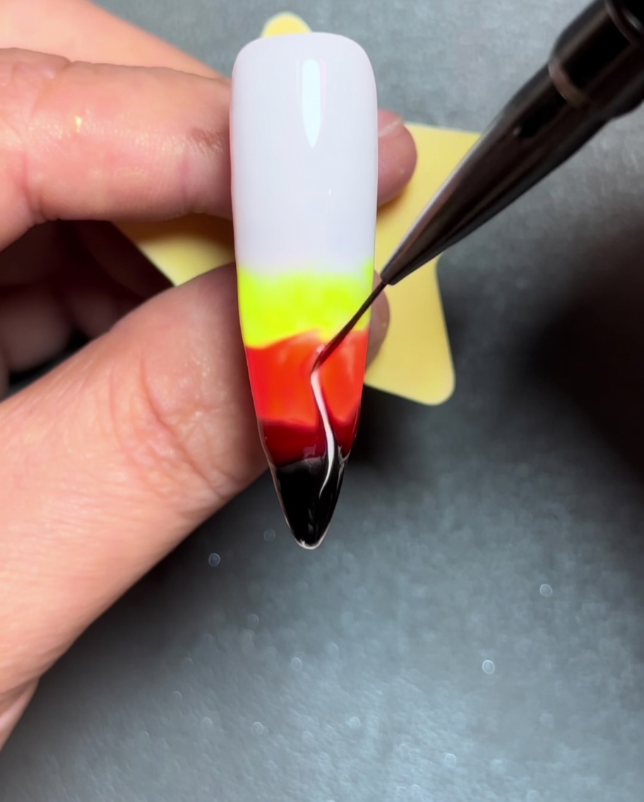 Eine Nahaufnahme, die zeigt, wie ein Liner-Pinsel Farblinien nach oben durch das nasse Gel zieht und so Flammenformen kreiert.