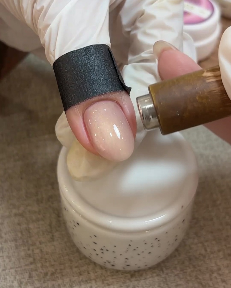 Nahaufnahme eines Magneten über einem Nagel mit noch nicht ausgehärtetem Cat-Eye-Gel, bei dem sich die Partikel zu einem hellen Lichtstreifen formen.