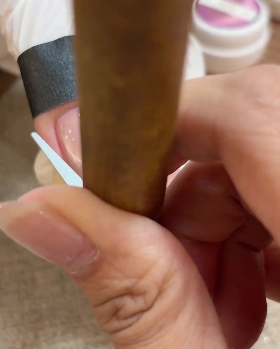 Nahaufnahme eines kleinen Werkzeugs, das das Cat-Eye-Gel in einen perfekten French-Tip-Bogen auf dem Nagel formt.