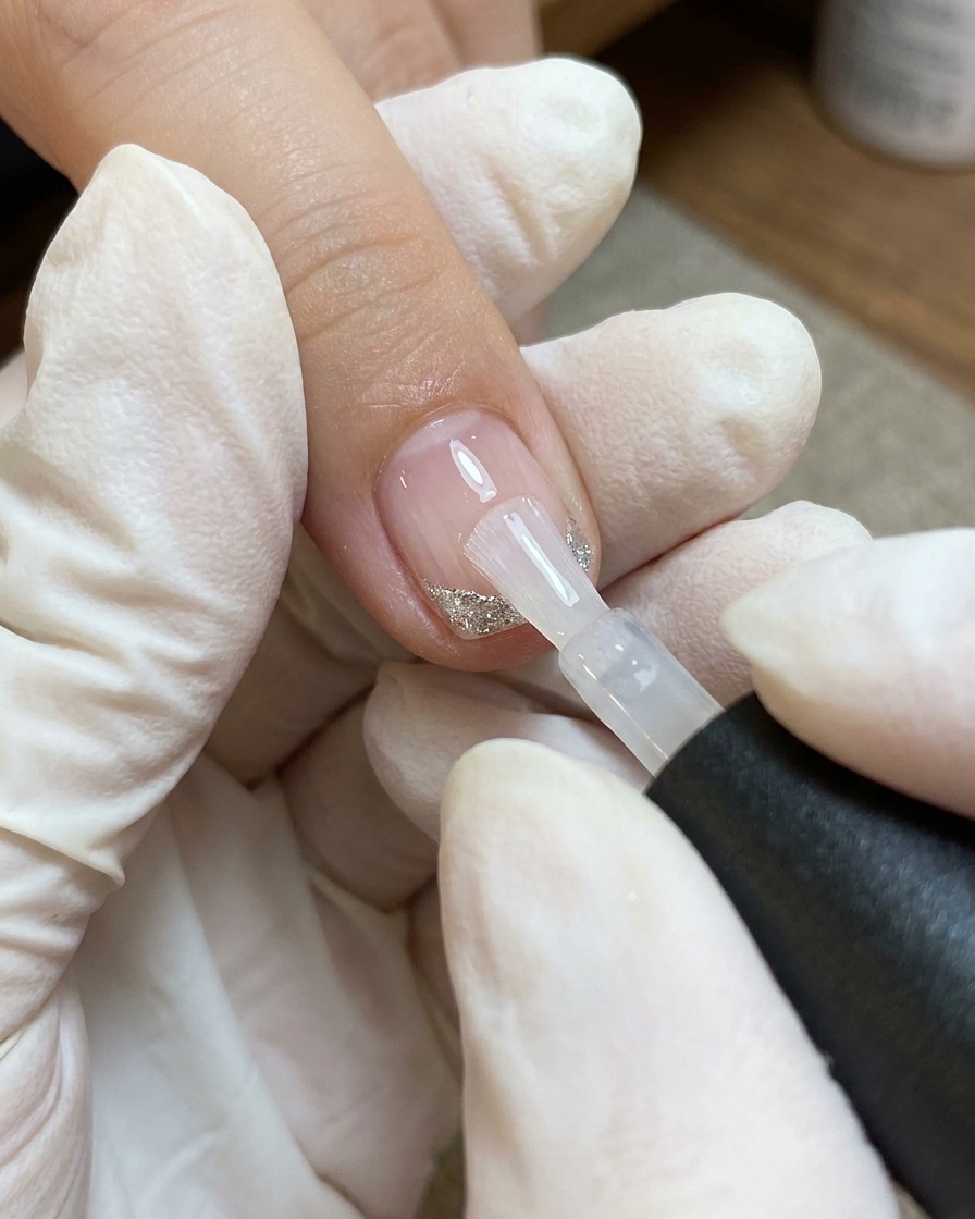 Ein Pinsel trägt eine Schicht klaren Top Coat auf den Nagel mit Herz und Linien auf.