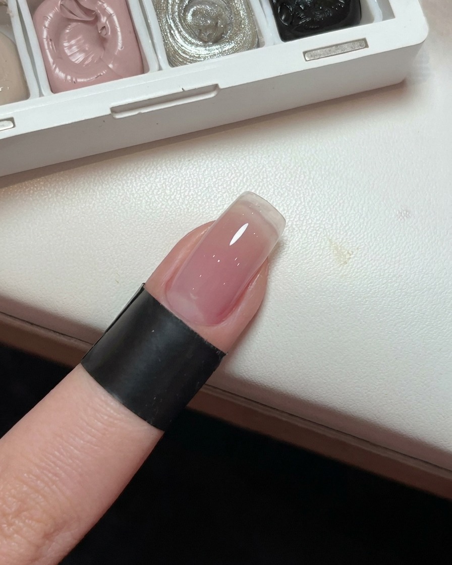 Nahaufnahme eines Fingernagels mit einem sanften, hellrosa Gel-Farbverlauf.