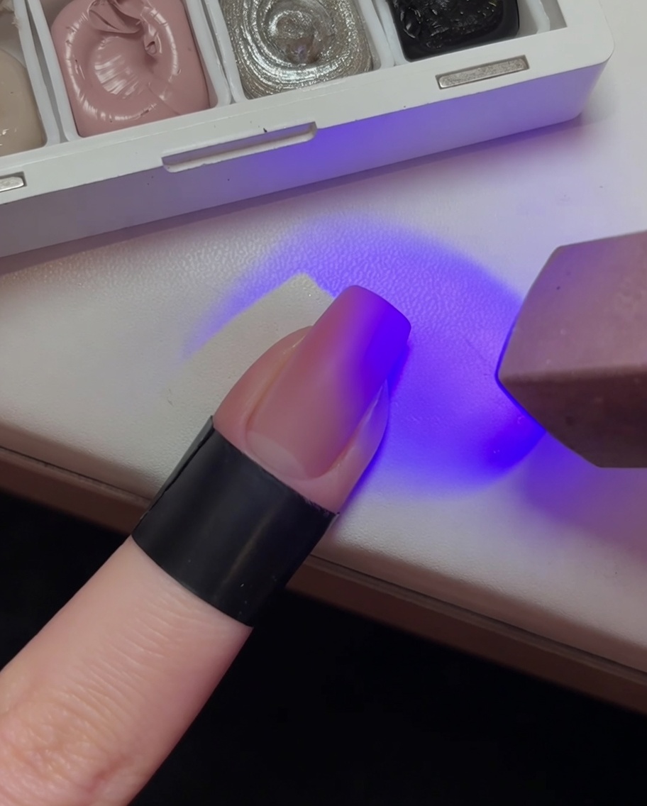 Ein Fingernagel mit rosa Farbverlauf unter dem violetten Licht einer UV-Lampe.