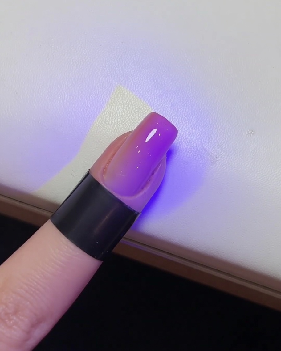 Ein glänzender, fertig gestellter Nagel während der Aushärtung in einer UV-Lampe.