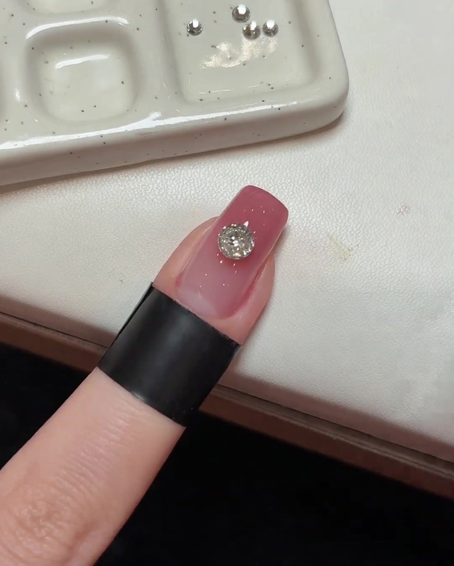 Der mittig platzierte Kristall auf dem rosa Nagel wird unter UV-Licht fixiert.
