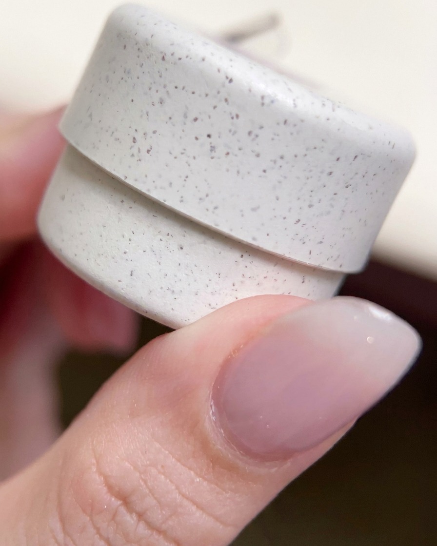 Nahaufnahme eines dekorativen, gesprenkelten Gel-Nagellacktiegels, der zwischen den Fingern gehalten wird.