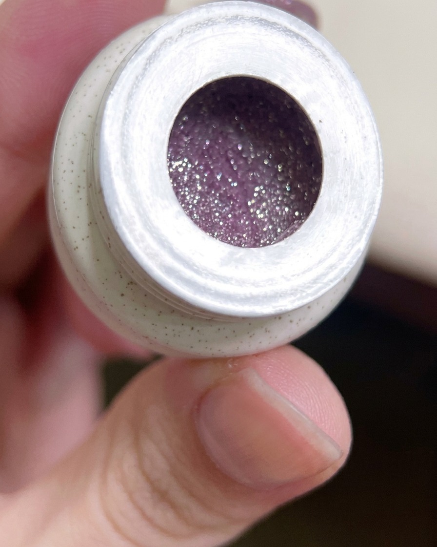 Ein flacher Gelpinsel taucht in einen Tiegel mit leuchtend glitzerndem, violettem Gel-Nagellack.