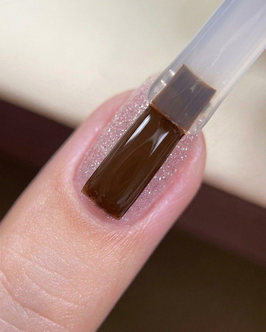 Ein Gelpinsel trägt einen klaren, glänzenden Top Coat auf einen mit Glitzer überzogenen Nagel auf.