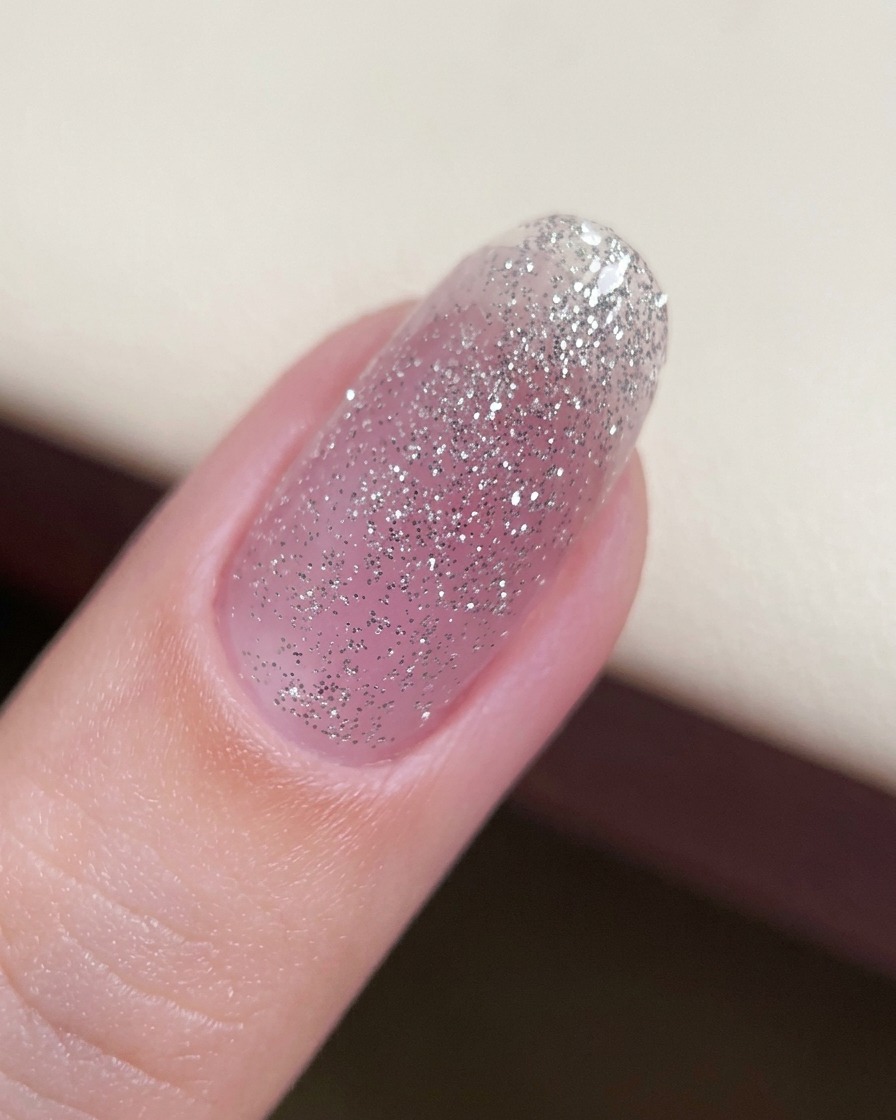Nahaufnahme eines Fingernagels mit einer dünnen Basisschicht aus Glitzergel.