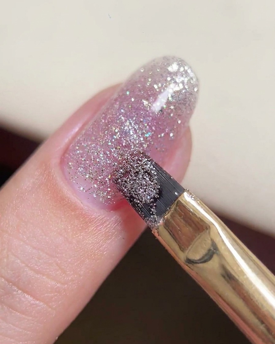 Ein Gelpinsel manipuliert eine größere Perle aus Glitzergel in der Mitte des Nagels.
