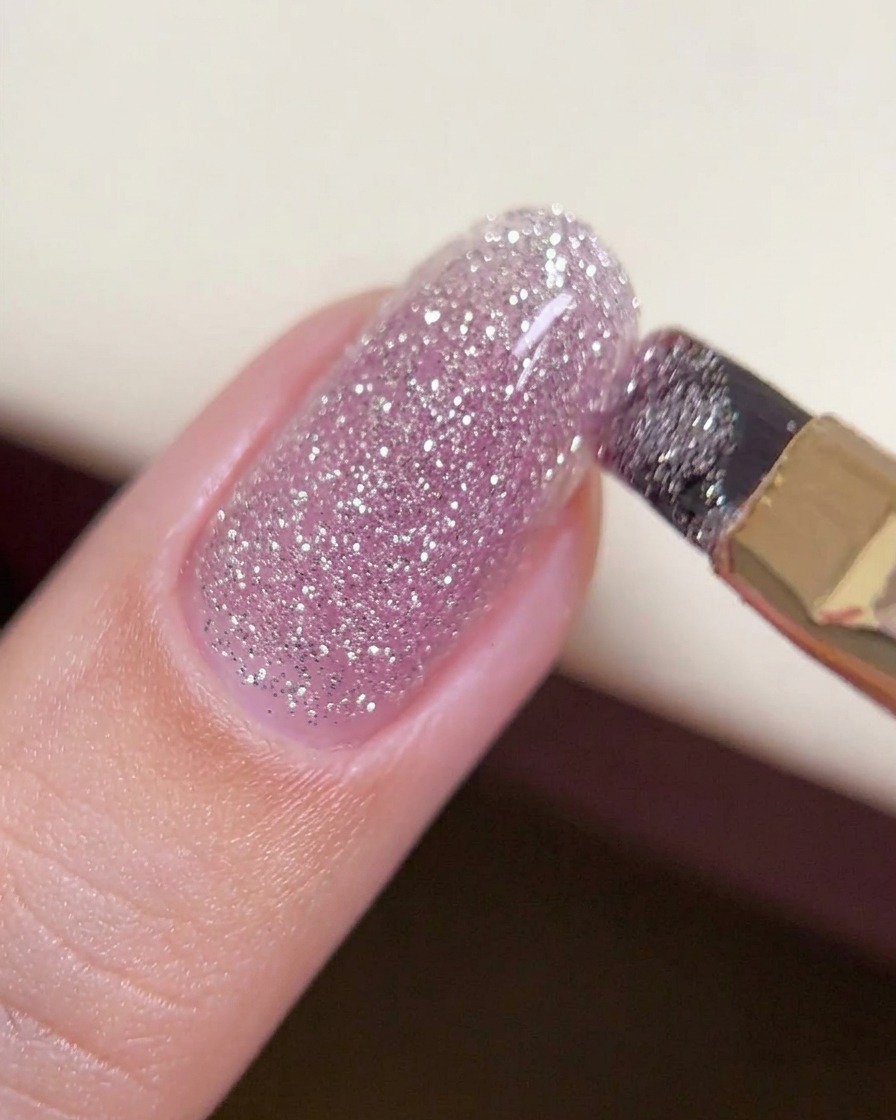 Ein Pinsel gleitet über eine dickere Perle Crush-Diamond-Gel in der Mitte eines Nagels, um eine gleichmäßige, strukturierte Schicht zu bilden.