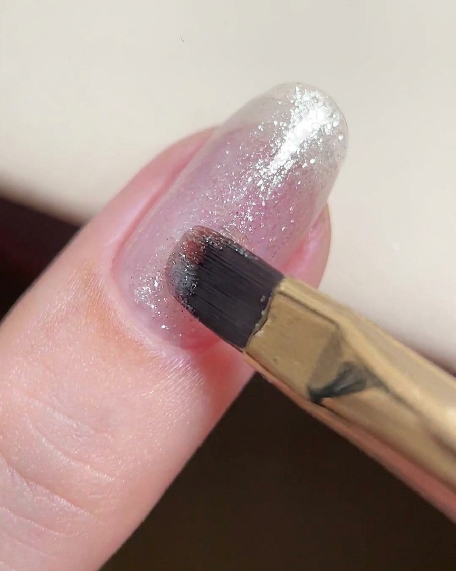 Ein Gelpinsel trägt eine dünne, konsistente Schicht aus feinem Silber-Glitzergel auf einen Naturnagel auf.