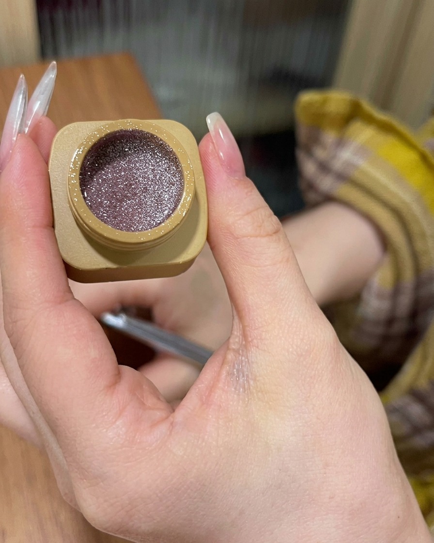 Nahaufnahme, wie pinkfarbenes Glitzergel auf die Nagelbasis aufgetragen und nach unten verblendet wird.