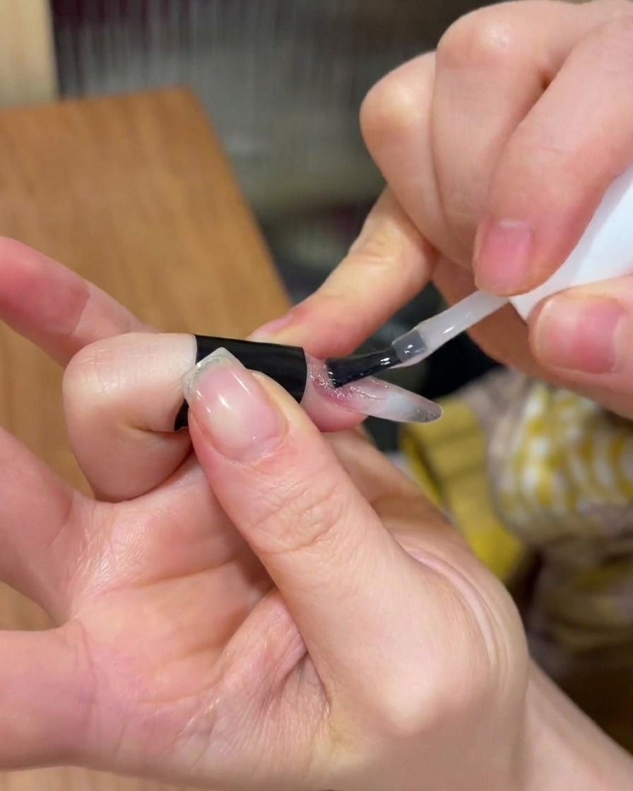 Das Auftragen einer klaren Schicht Aufbaugel über das bestehende Nageldesign.