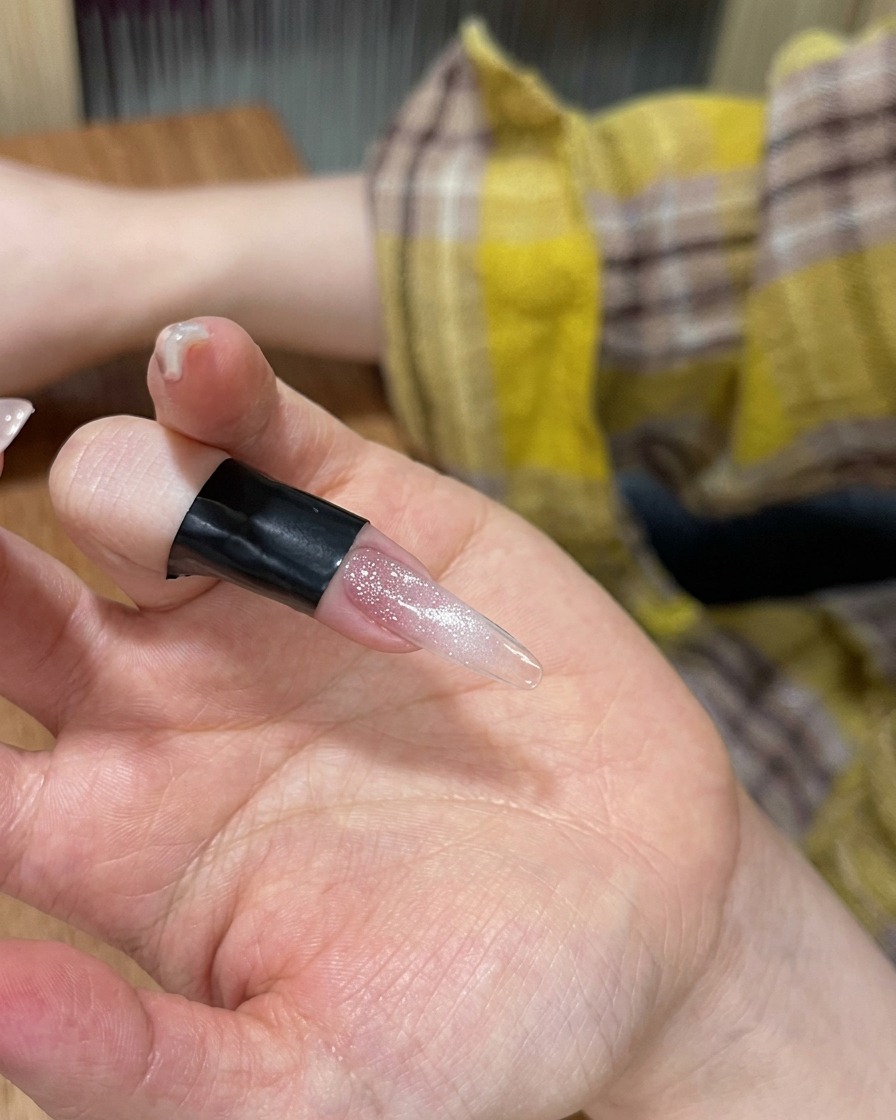 Nahaufnahme eines Fingers mit Cat-Eye-Gellack, der in einer tragbaren LED-Lampe liegt.