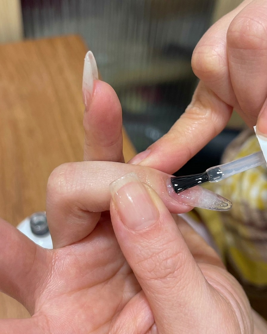 Ein Pinsel trägt einen klaren, glänzenden Top Coat über einen texturierten Cat-Eye-Nagel auf.