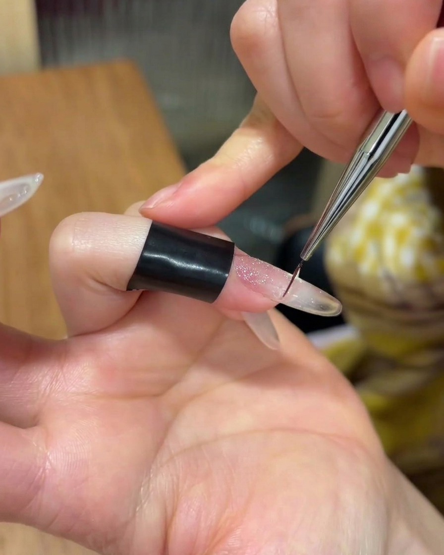 Eine kleine Menge klares Klebegel wird auf die Mitte eines manikürten Nagels aufgetragen.
