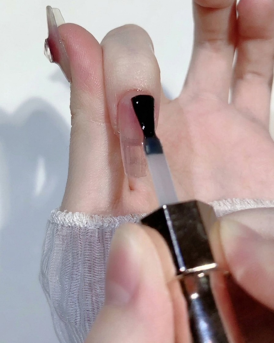 Ein kleiner Tropfen transparentes rosa Blush-Gel wird in der Mitte eines klaren Nageltips aufgetragen.