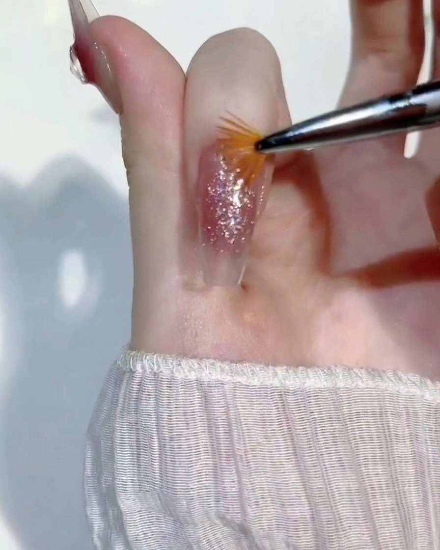 Ein Miniatur-Fächerpinsel wird leicht über eine feuchte Schicht Glitzergel auf einem Fingernagel gestrichen, um die Deckkraft auszugleichen.