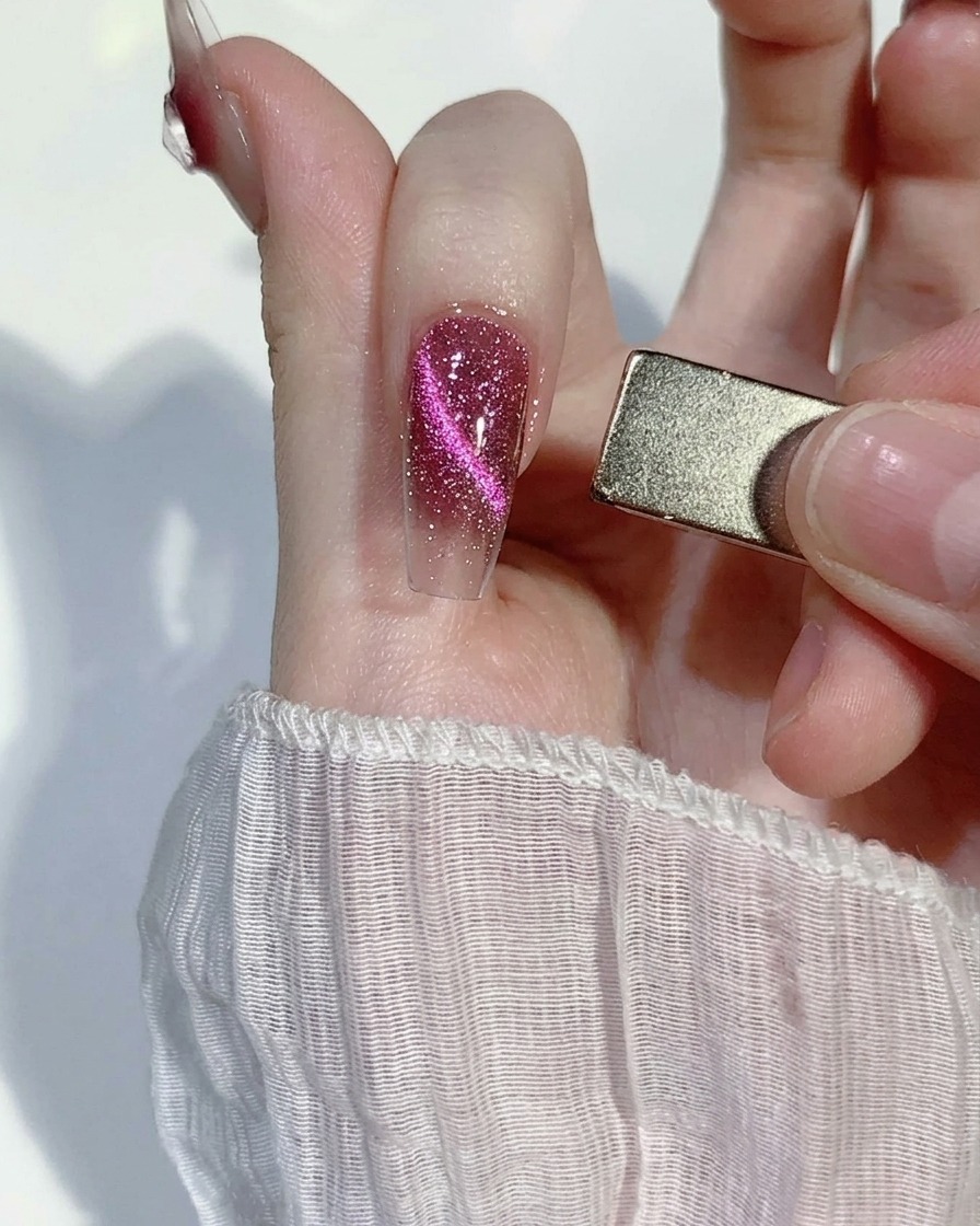 Ein rechteckiger Nagelmagnet wird an die Seite eines rosa Glitzernagels gehalten und zieht die magnetischen Partikel in eine fokussierte Linie.