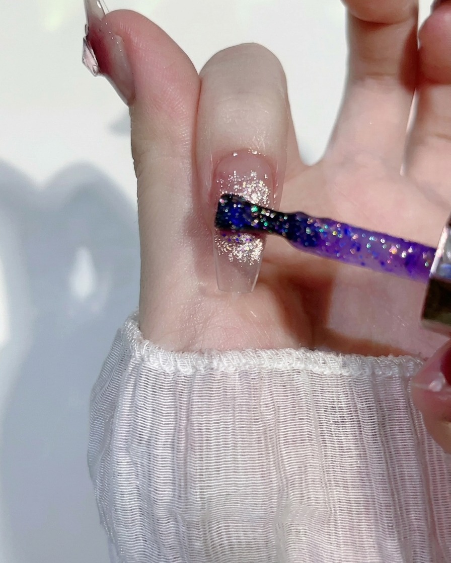 Eine dünne Schicht lilafarbenes, glitzerndes Gel wird über ein bestehendes rosa Cat-Eye-Nageldesign gestrichen.