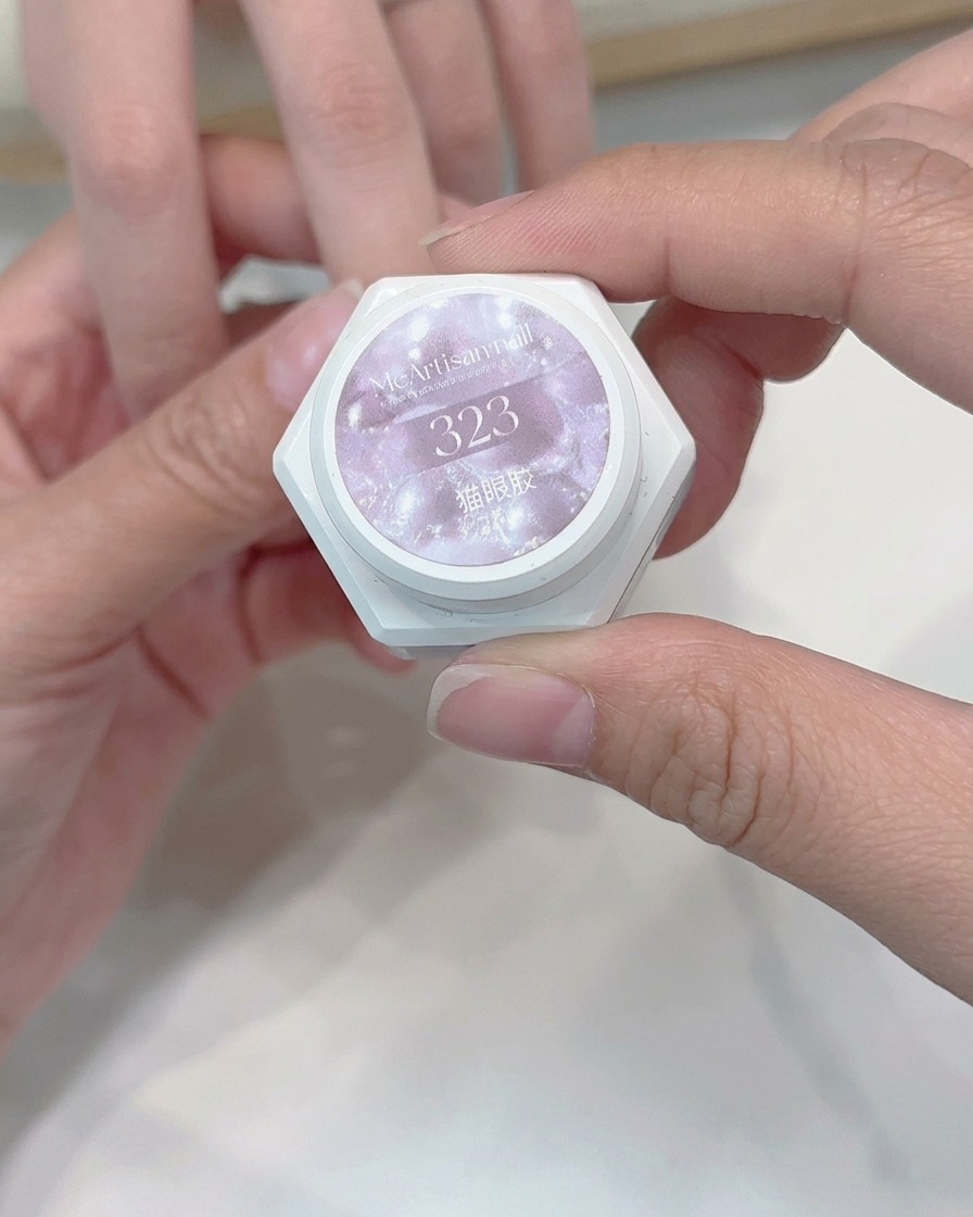 Ein Pinsel trägt eine Schicht helles Cat-Eye-Gel auf einen Nagel auf.