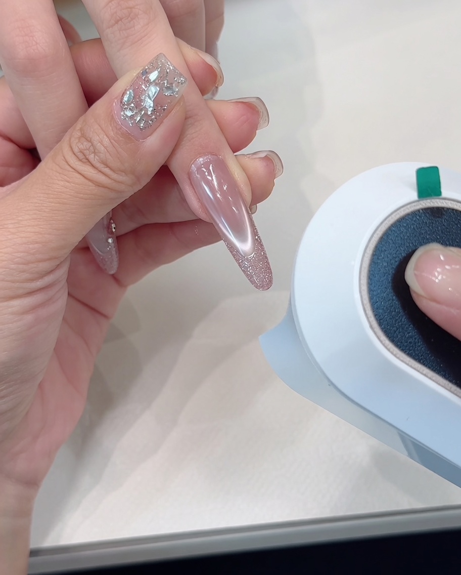 Eine Hand liegt unter einer UV/LED-Lampe, der Fokus liegt auf den Nägeln mit Glitzerspitzen.