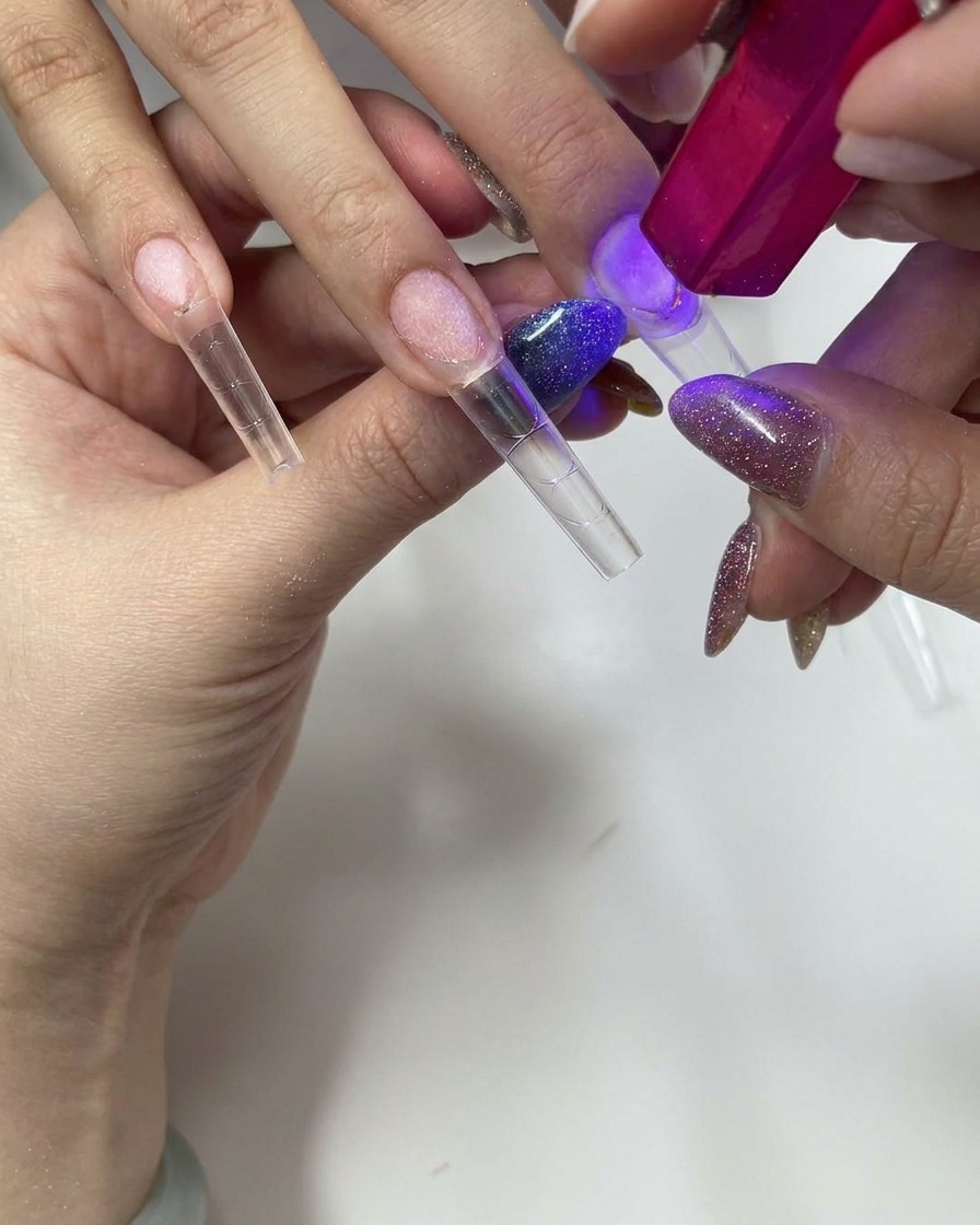 Verwendung einer kleinen pinken UV/LED-Handlampe zum Aushärten des transparenten Nageltips.
