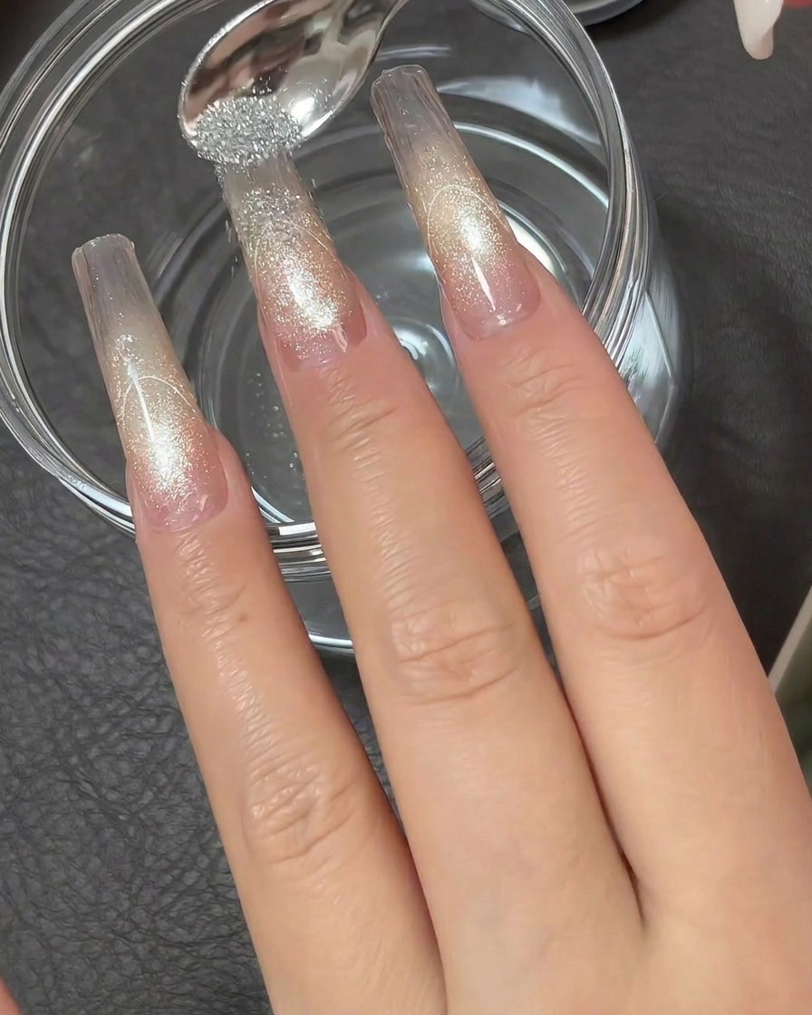 Ein kleiner Metalllöffel lässt hochreflektierendes silbernes Diamant-Puder über die klebrige Spitze einer klaren Nagelverlängerung rieseln.