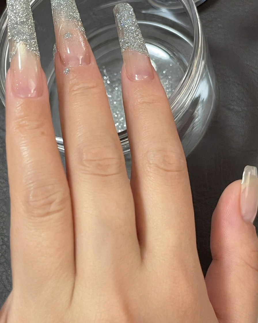 Nahaufnahme eines Fingers, der leicht geklopft wird, um loses Glitzerpuder von der Nagelspitze zu schütteln.