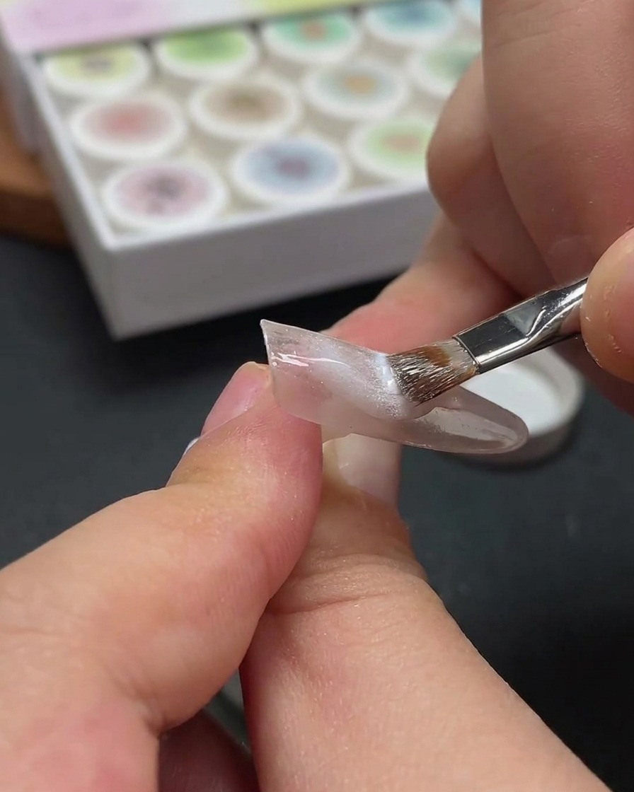 Nahaufnahme eines magnetischen Werkzeugs, das über einem Fingernagel schwebt, um die Metallpartikel im feuchten Gel zu verschieben.