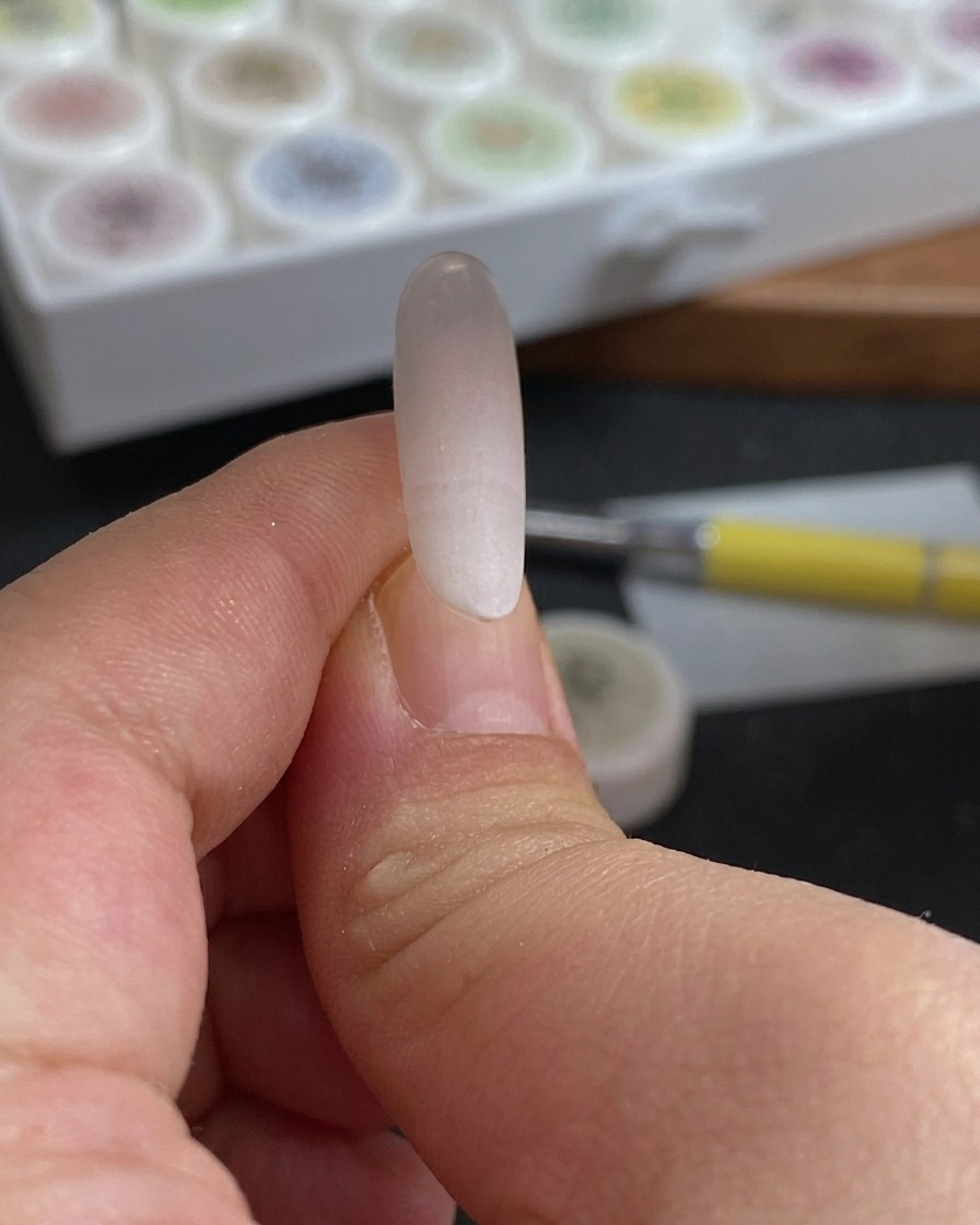 Nahaufnahme eines Schwamms, der auf eine Nagelspitze getupft wird, um einen sanften rosa-weißen Farbverlauf zu erzeugen.