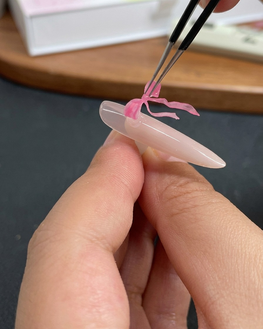 Eine Pinzette platziert ein filigranes rosa Schmetterlings-Charm auf einen mit klarem Gel beschichteten Fingernagel.