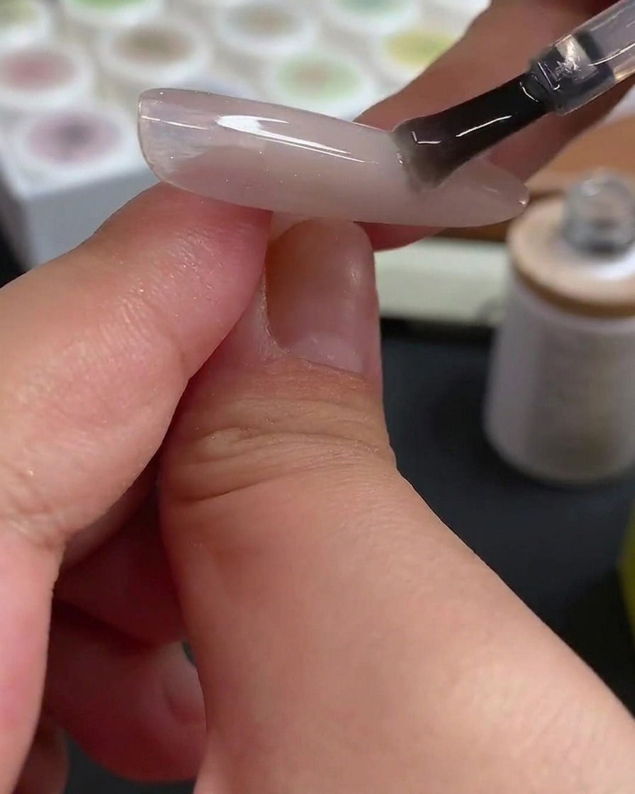 Ein Dotting-Tool setzt präzise rosarote Gelpunkte auf eine vorbereitete Nageloberfläche.