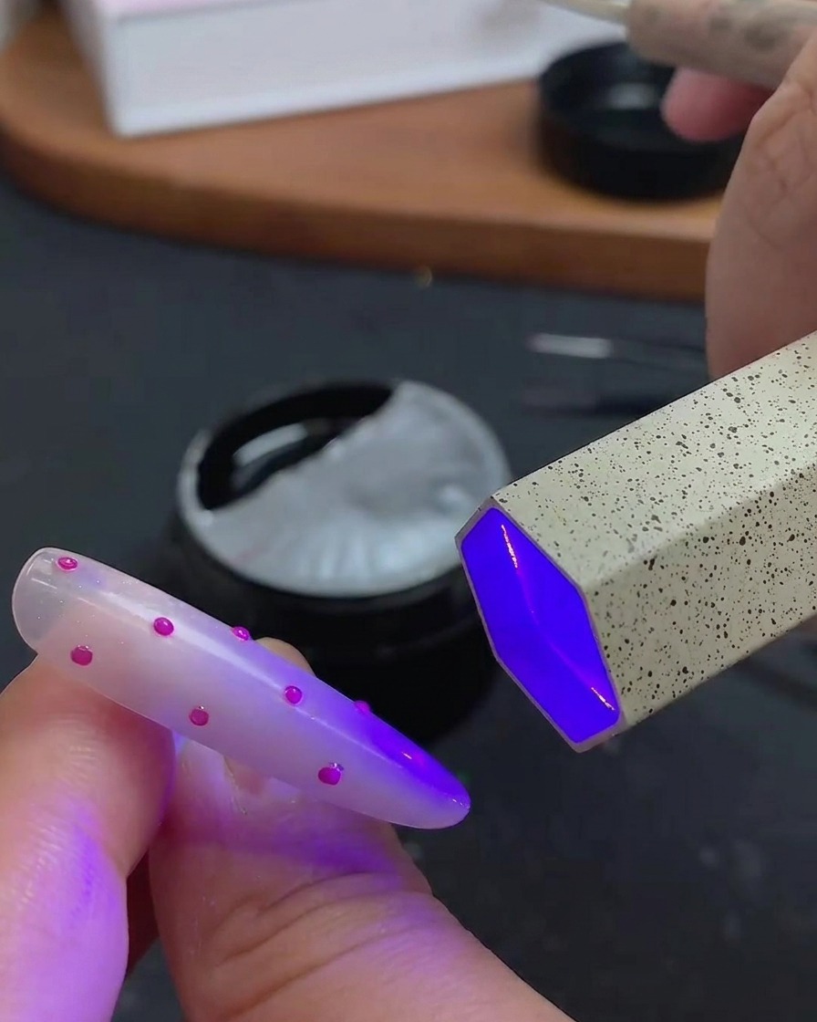 Ein Pinsel trägt einen klaren, glänzenden Überlack über die 3D-Punkt-Nailart auf.