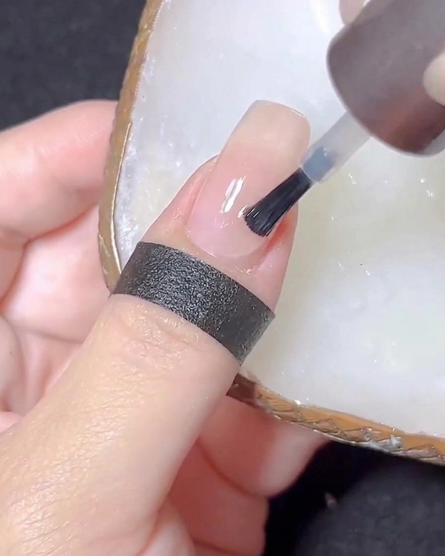 Ein Nagelpinsel trägt einen klaren Top Coat auf einen nudefarbenen Nagel auf.