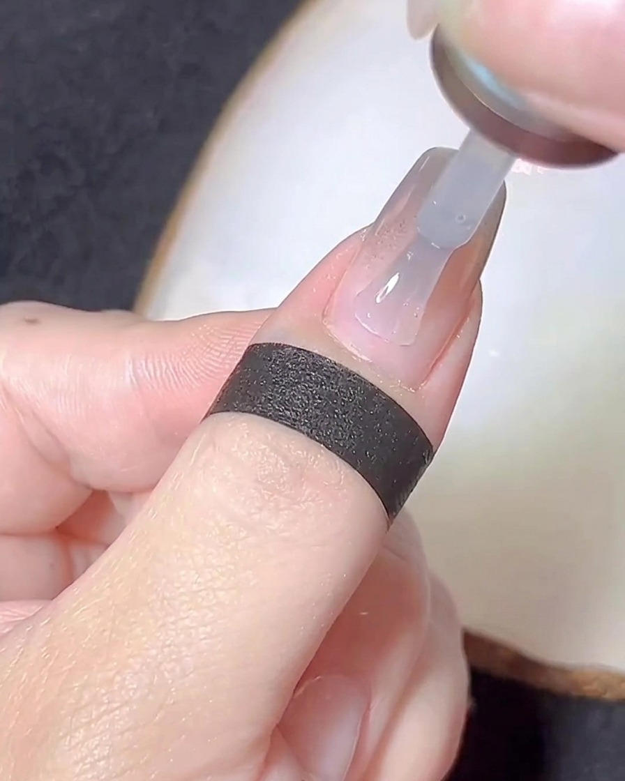 Ein Pinsel trägt eine dünne Schicht klares Basisgel über einen mit Chrome-Puder bedeckten Nagel auf.